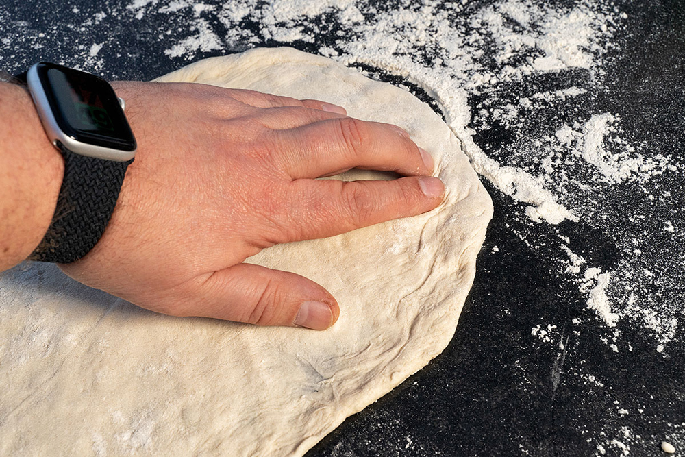 Pizzastein vorheizen. Brenner auf mittlere Hitze zurückdrehen. 
      Teigling mit bemehlten Fingern kreisrund formen. Äußeren Rand nicht festdrücken.