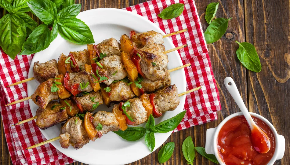 Saftig gegrillte Schaschlik Spieße auf einem weißen Teller, serviert mit roter BBQ-Sauce, die auf Basis einer würzigen Schaschlik Marinade zubereitet wurde.