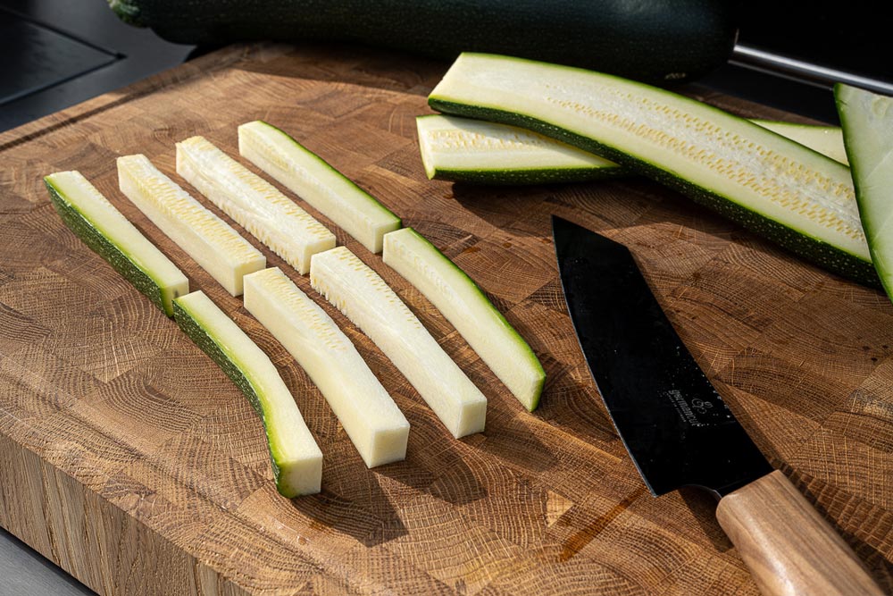 Die Zucchini längs in ca. 1,5 cm breite Scheiben und anschließend jeweils
in 4 Stifte schneiden und anschließend in der Mitte teilen.