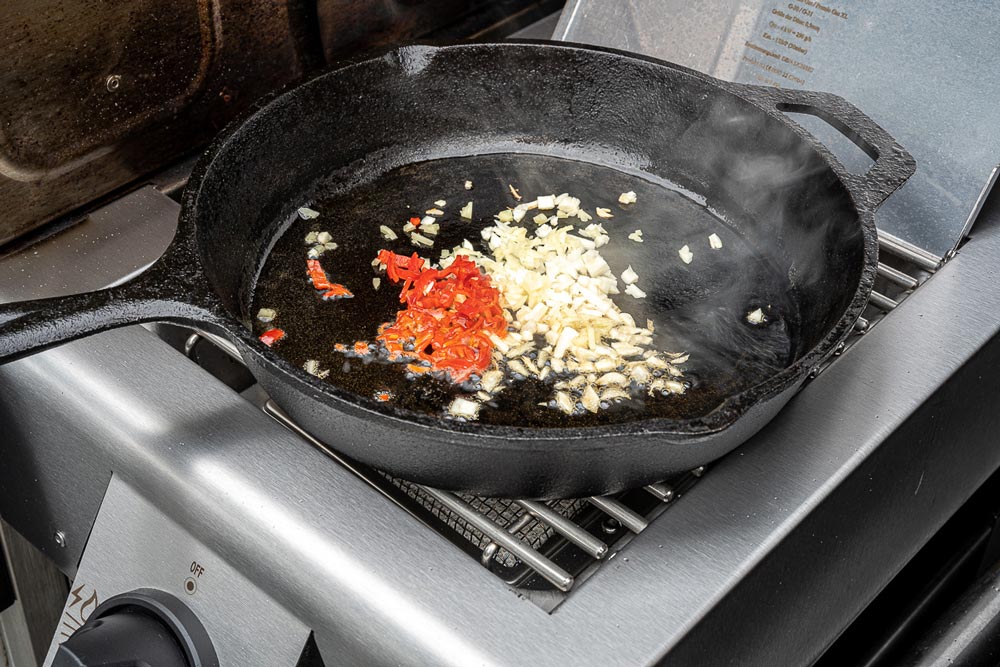 Chili, Knoblauch und Ingwer in einer gusseisernen Pfanne mit etwas Sesamöl auf dem 
        Seitenbrenner kurz anbraten