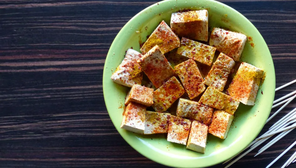 In Würfel geschnittene Tofustücke, die auf einem grünen Teller mit einer würzigen Tofu-Marinade.