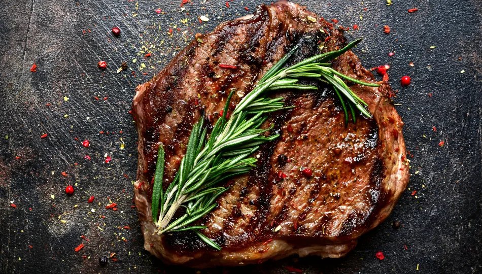 Ein auf den Punkt gegrilltes Steak auf einer dunklen Steinplatte, roter Pfeffer und ein paar Kräuter verfeinern die Optik. Eine leckere Steak Marinade gibt den perfekten Geschmack.