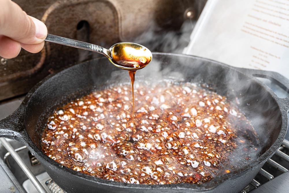 Braunen Zucker in die Marinade einrühren, Speisestärke hinzufügen und so lange köcheln lassen, bis die Marinade dickflüssig wird.